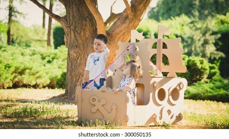 Boy and girl playing in a cardboard boat in the park. Eco concept
