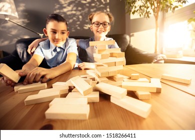 Boy And Girl Are Playing Jenga While Sitting In The The Living Room Near The Window.