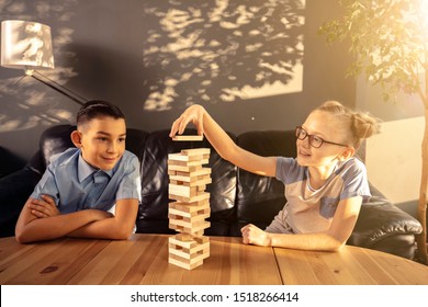 Boy And Girl Are Playing Jenga While Sitting In The The Living Room Near The Window.