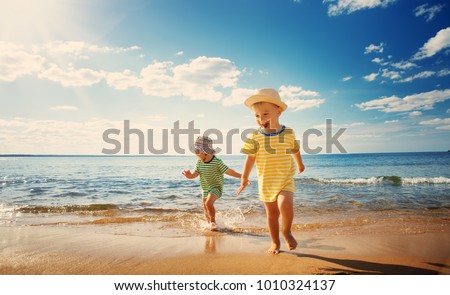 Boy and girl playing on the beach on summer holidays. Children in nature with beautiful sea, sand and blue sky. Happy kids on vacations at seaside running in the water