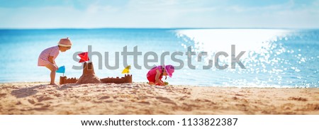 Boy and girl playing on the beach on summer holidays. Children building a sandcastle at sea