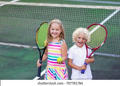 Boy And Girl Playing Tennis On Outdoor Court. Kids With Tennis Racket And Ball In Sport Club. Active Exercise. Summer Activities For Children. Training For Young Kid. Child Learning To Play