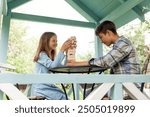 boy and a girl are playing with wooden blocks, under the roof of a gazebo. The sister holds the top of the tower, preventing it from falling, while her brother carefully pulls out the block from the