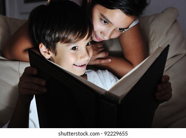 Boy And Girl Reading Light Book At Night, Children Concept