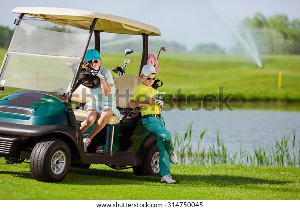 Boy and girl resting near golf car at golf course at\
summer day