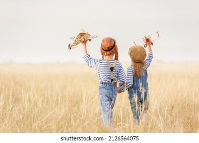 Boy and girl are running on the grass in the open air. Cheerful and happy children play in the field and imagine themselves to be pilots on a sunny summer day. Kids dreams of flying and aviation.