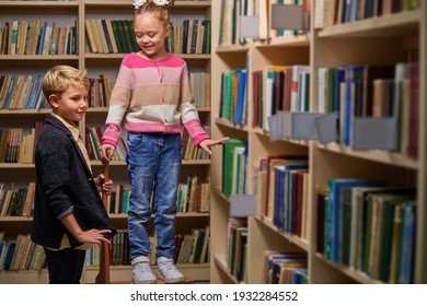 boy and girl stand talking in library, discussing books, choose books for school. stand between bookshelves