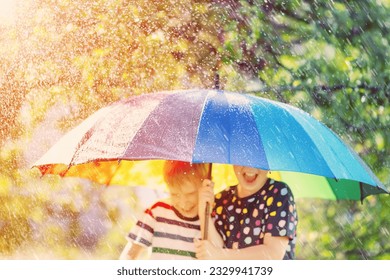 Boy and girl standing outdoors in rainy day under colourful umbrella. Concept of the friendship and childhood. - Shutterstock ID 2329941739
