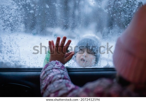 Boy and\
girl touch each other with their palms through the frozen car\
window, winter road trip with the whole family, active weekend in\
any weather, winter car safety, help and\
support
