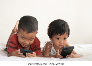 A boy and a girl, two siblings Lying down and looking at his cell phone on the bed in his house. The concept of love and warmth in the family - Powered by Shutterstock