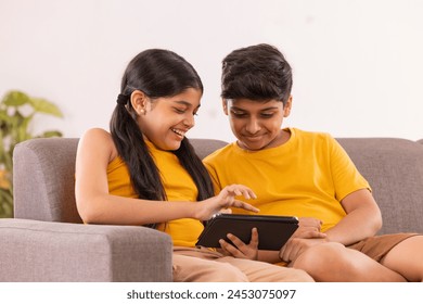 Boy and girl using digital tablet while sitting on sofa in living room - Powered by Shutterstock