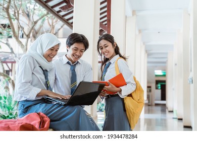 A Boy, Girl, And Girl In A Veil In High School Uniform Doing Group Assignment Using A Laptop Computer Together