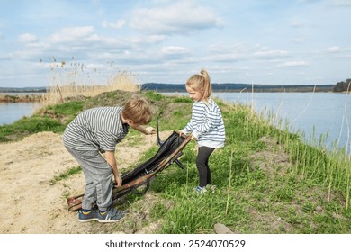 Boy and girl work together to unpack fishing rod by riverbank, preparing for day of outdoor fun and fishing. - Powered by Shutterstock