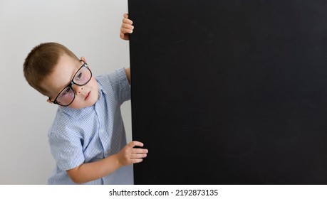 A boy in glasses and a blue shirt holds a blackboard with his hands - Shutterstock ID 2192873135