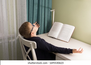 boy in glasses and a jacket sits at a table and does a school task