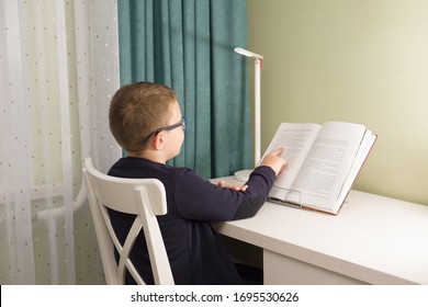 boy in glasses and a jacket sits at a table and does a school task