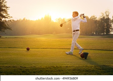 Boy golf player hitting by iron from fairway at sunset
