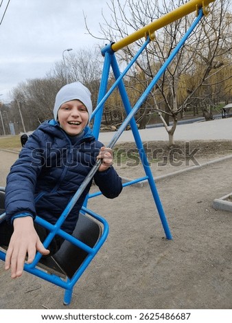 A boy in a gray hat and a blue jacket is riding on a swing