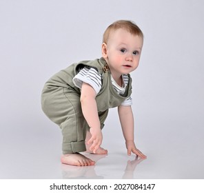 boy in a green casual overalls, barefoot, squatted down, but noticed something interesting upstairs, froze in anticipation, leaning with one hand on the floor.