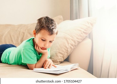 Boy in green t-shirt reading a book at home on sofa. Distance learning education. Digital detox. Boy in quarantine stay at home in self isolation.