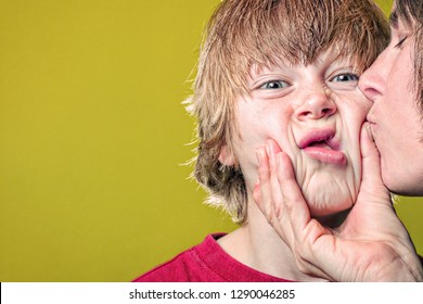 Boy grimacing when his mother grabs his face while kissing him
