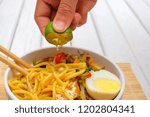 Boy hand squeezing lime on Malay Mee Rebus in the bowl  with chopsticks on white table This dish is made of noodles ,vegetable,egg with a spicy .