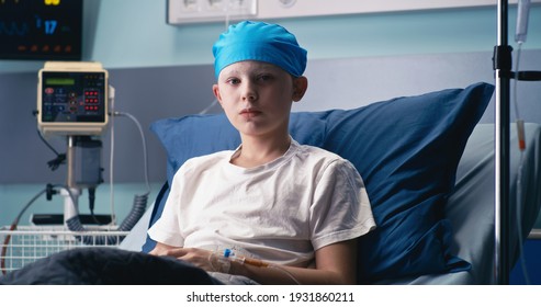 Boy In Hat Looking At Camera While Lying On Bed In Ward Of Modern Cancer Hospital