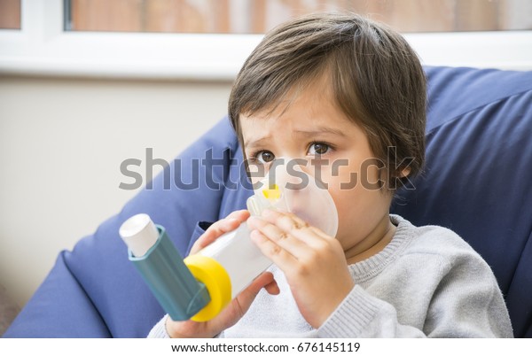 A boy have a problem with chest\
coughing holding inhaler mask by him self, Kid using the volumtic\
for breathing treatment, Healthcare and medicine\
concept