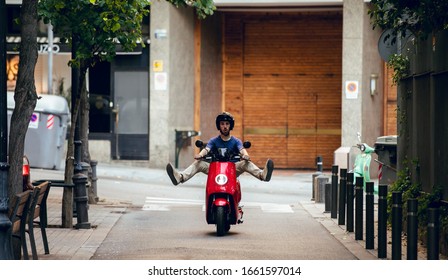 boy having fun driving red motorcycle through barcelona city in summer by street