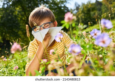 Boy with hay fever sits in a blooming meadow while sneezing with a handkerchief