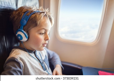 Boy With Headphones Watching And Listening To In Flight Entertainment On Board Airplane