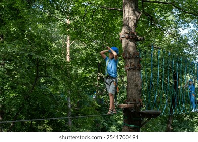 Boy in helmet balancing on ropes course in forest adventure park on sunny day. Concept of outdoor activities, children adventures and an active lifestyle in nature. High quality photo - Powered by Shutterstock