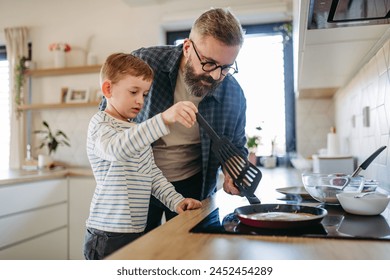 Boy helping father to make pancake. Father spending time with son at home, making snack together, cooking. Fathers day concept. - Powered by Shutterstock