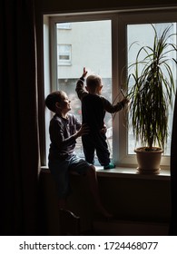 boy helps his little brother to stand on the windowsill and look out the window. older brother supports his younger on the windowsill.Warm relationship between brothers. children at home. 