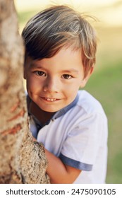 Boy, hide and happy by tree for portrait in park for games, adventure and outdoor for playing in summer. Child, nature and shy smile in forest for holiday, vacation and freedom for growth in Canada