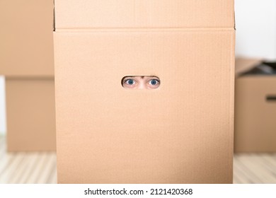 Boy Hiding In Inside A Huge Cardboard Box. He Is Playing And Peeking Through A Hole In Box. Kid Is Happy About Moving Into A New Home.