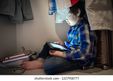 Boy hiding in a wardrobe to look at his digital tablet