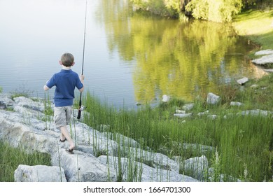 A Boy With His Fishing Rod On The Shore Of A Lake Or River.