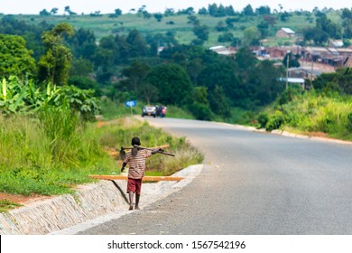 A Boy With A Hoe Is Walking Down A Street In Uganda