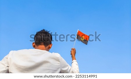 Boy holding Angola flag against clear blue sky. Man hand waving Angolan flag view from back, copy space for text