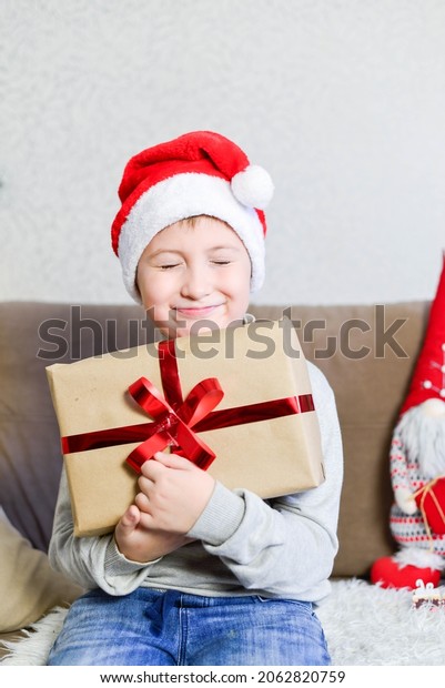 A boy is holding Cristmas gift. He is happy.\
Vertical frame.