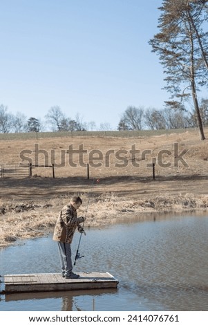 boy holding fishing rod on dock in pond