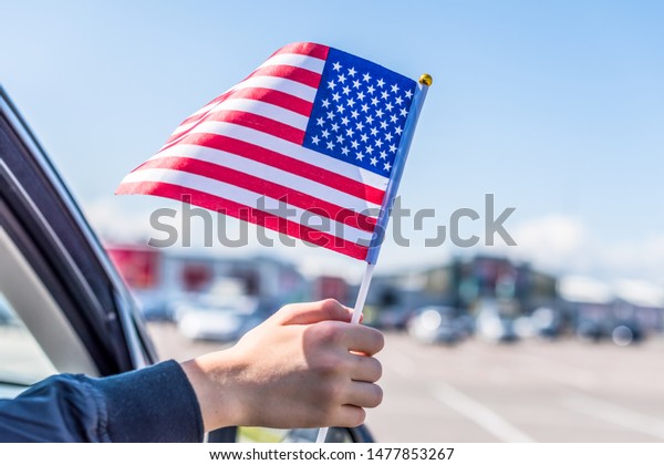 Boy holding Flag of\
America from the open car window on the parking of the shopping\
mall. USA.Concept