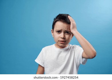 Boy holding his temple. Facial emotion on blue background with copy space - Shutterstock ID 1927458254