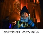 Boy holding a house with the Holy Family, newborn Jesus and a candle. Portrait of a child in front of a Catholic church after Christmas mass.