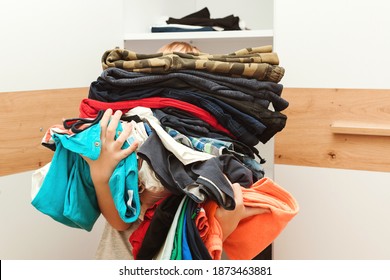 Boy holding a huge pile of clothes. Kid makes order in the closet. Storage organization. Second hand kids clothes for reusing, reselling, recycling and donatation.