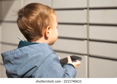 Boy Holding Mobile Phone Near To Parcel Locker Collecting Parcel From Shopping Locker. Child Skans QR Code On Mobile Phone Self-service Locker Cell With Bar Code Reader Modern Shipping Concept