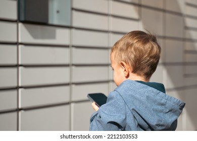 Boy Holding Mobile Phone Near To Parcel Locker Collecting Parcel From Shopping Locker. Child Skans QR Code On Mobile Phone Self-service Locker Cell With Bar Code Reader Modern Shipping Concept