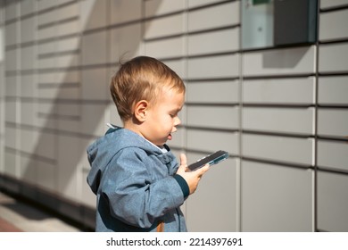 Boy Holding Mobile Phone Near To Parcel Locker Collecting Parcel From Shopping Locker. Child Skans QR Code On Mobile Phone Self-service Locker Cell With Bar Code Reader Modern Shipping Concept.