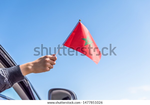 Boy holding Morocco Flag from the\
open car window on the sky background.\
Concept